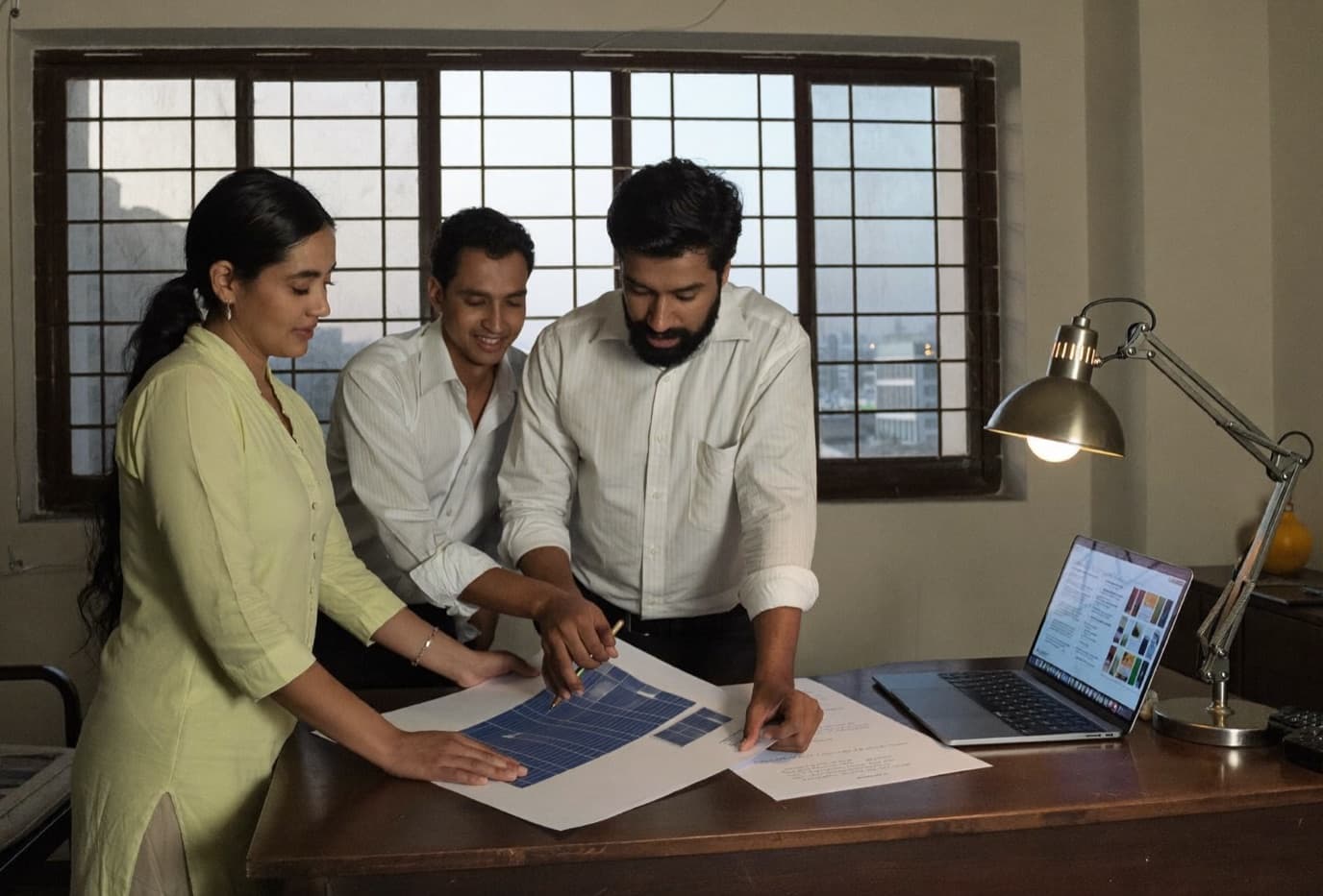 A small solar sales team reviewing a rooftop panel layout and proposal around a work table